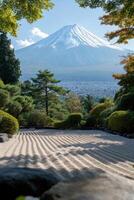 Snowy mountain peak viewed from zen garden with raked sand and green trees under a blue sky in peaceful scene. photo