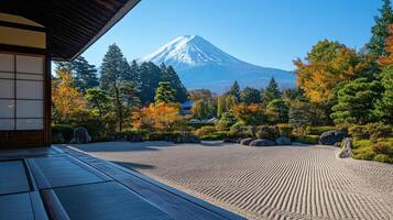 Zen garden with raked sand leads toward colorful trees and a snow capped mountain under clear blue sky viewed from building veranda. photo
