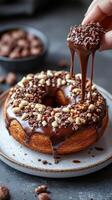 Delicious donut with chocolate glaze and sprinkles. Hand dips cake piece in chocolate. Sweet treat on plate on dark surface. Food close up. photo