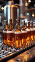 Amber bottles filled with liquid stand on a metal conveyor in a factory setting with brewing equipment and lights visible behind. photo