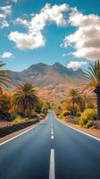 Asphalt road stretches toward mountains under bright sky. Palm trees and green bushes line roadside in warm light. Peaceful landscape with travel feel. photo