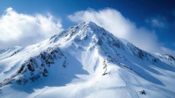 Snowy mountain peak under blue sky. White clouds above the cold mountain. Traces in the fresh winter snow. Cold scenery background. photo