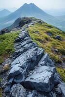 Rocky mountain ridge leading to distant peak. Green plants grow along the rocky path. Mountain range fades into the background. Outdoor scene. photo