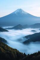 Snowy mountain peak rises above a sea of white clouds. Green forest and rolling hills sit in the valley below against a blue sky. photo