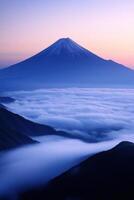 Snowy mountain peak rises above a thick layer of clouds during a colorful sunrise. Distant hills frame the lower part of the image. photo