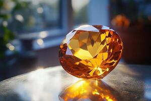 Orange gemstone rests on a reflective surface. Light shines through the facets. A window and greenery are blurred in the background. photo