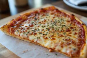 Single pizza slice with melted cheese and herbs on a wooden board and white paper. Pizza displays red sauce and a golden crust. photo