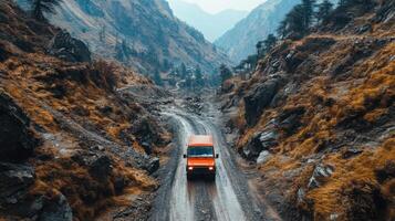 Orange vehicle drives on rough mountain road. Steep slopes with autumn colored vegetation line the path through tall hills. photo