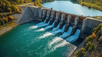 Concrete dam holding back turquoise lake. Water flows strongly through opened gates. Forest colors are seen on the surrounding hills. Early autumn season. photo