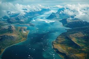 Aerial view of a glacier flowing into ocean waters. Mountains rise along the coast. Icebergs float in the deep blue water under cloudy skies. photo