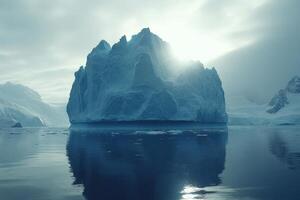 Large blue iceberg floats in cold ocean water. Sunlight shines behind the ice formation. Distant snowy mountains in background. Reflections on dark water. photo