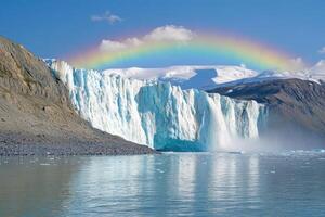 Glacier face meets the sea with rainbow above. Waterfalls cascade from the ice face. Mountains rise with snow against a blue sky. photo