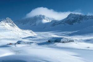 Snowy mountains surround buildings on a flat plain. Blue sky and clouds cover some peaks. Winter landscape shows pristine white snow everywhere. photo