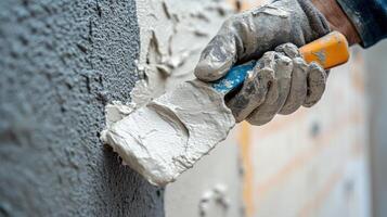 Hand in glove applying stucco to gray wall with spatula tool. White plaster spreading on surface. Home improvement, construction work closeup detail. photo