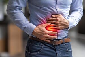 Man holds abdomen in pain. Bright red glow indicating sore area. Light blue shirt and blue jeans with brown belt. Healthcare related. photo