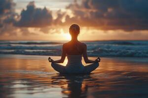 Woman meditates on beach at sunset. Ocean waves break gently in background. Calm peaceful serene nature scene. Sunlight reflections shimmer on sand. photo