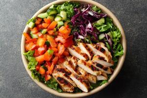 Top down view of a bowl with mixed salad and grilled chicken. Red bell peppers and sliced cucumbers with red cabbage on lettuce. photo