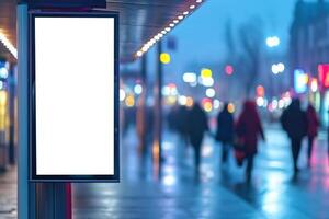 Blank advertisement display at bus stop. People walking by in the blurred background. City street with lights in the evening. Empty billboard template. photo