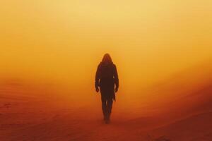 Person with hood walks alone in desert sand. Orange fog covers ground during the day. Walking figure with backpack faces forward. photo