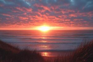 Bright sunset over ocean horizon. Waves gently rolling onto sandy beach. Grasses in foreground. Clouds reflect orange and red light. photo