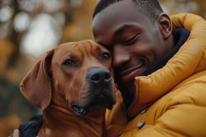 Close up of brown dog being embraced by person wearing yellow coat in outdoor fall setting with soft focus leaves behind photo