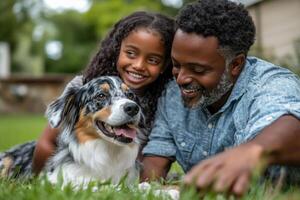 Girl and father play with dog. Happy family lie together on grass in the summer sun. Pet dog smiles happily. photo