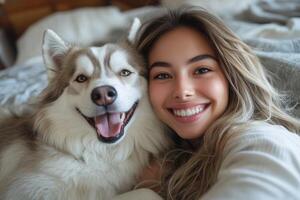 Smiling girl with long hair taking selfie with happy husky dog on a cozy bed. Pet love and friendship concept. photo