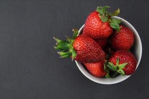 Strawberries lie in a gray bowl on a black background. Farm food. photo