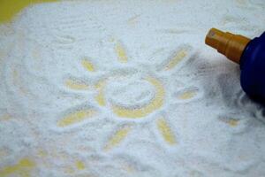 The sun is drawn on a sandy background, a bottle of protective oil is visible in the background. The concept of tourism, vacation, summer. photo