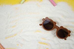 On a sandy background lie children's sunglasses surrounded by chalk for drawing. Concept of beach, summer, vacation photo