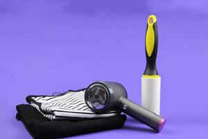 Two T-shirts are lying on a purple background, next to them is a lint machine and a clothes roller. Concept of caring about cleaning clothes. photo