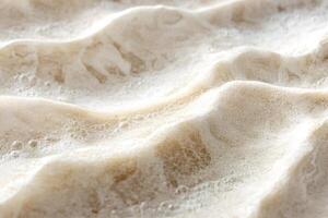 Soft sea foam creating textures on sandy beach photo