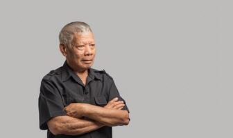 Portrait of an elderly Asian man in a shirt looking away with a smile while standing arms crossed on a gray background photo