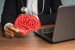 Doctor in a suit holding a brain symbol made from red paper while sitting at the table in the hospital photo