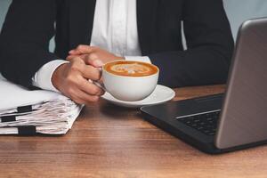 Close-up of businessman in a suit hand holding a cup of coffee while sitting working at the table photo