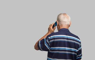 Back view of a senior man using a smartphone while standing on a gray background. Space for text. photo
