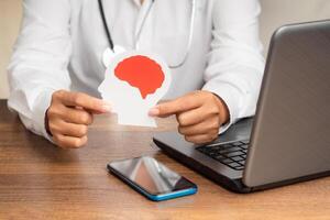 Close-up of a doctor in a uniform holding a brain symbol made from paper while sitting at the table. photo