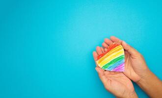 Rainbow heart paper symbol in hands on a blue background. Top view. photo