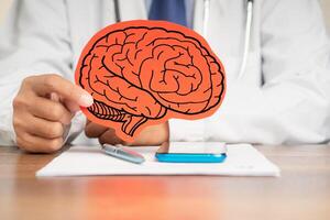 Doctor in a uniform holding a brain symbol made from red paper while sitting at the table. photo