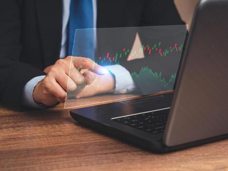 Hand of a businessman pointing at graph stock on a virtual screen while sitting at the table in the office photo