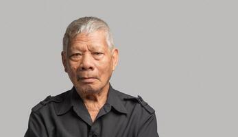 Portrait of an elderly Asian man in a shirt looking at the camera with a smile while standing on a gray background. photo