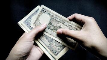 Low light concept of a man holding some old rupiah Rp.10 notes. Isolated on a black background, close up view photo