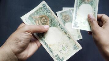 Portrait of a person's hand counting old rupiah banknotes of Rp500,00 isolated on a black background. photo