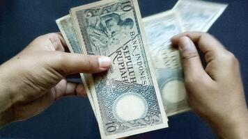 Close up view of a person's hand counting several old rupiah banknotes of Rp10,00 isolated on a black background. photo