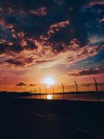 Sunset Over Water With Dramatic Clouds and Silhouetted Fence photo