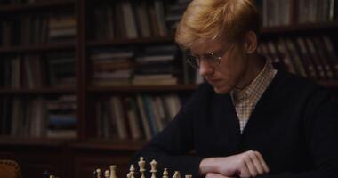 A man in glasses playing chess in front of a bookcase photo