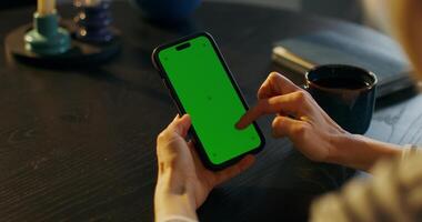 Woman using smartphone with green screen at table photo