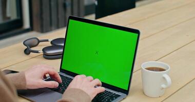 Man using laptop with green screen on wooden table photo