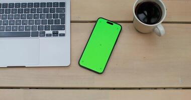 A green phone and a laptop on a wooden table photo