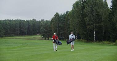 Rear view of two men walking across a golf course with gear bags on their backs photo